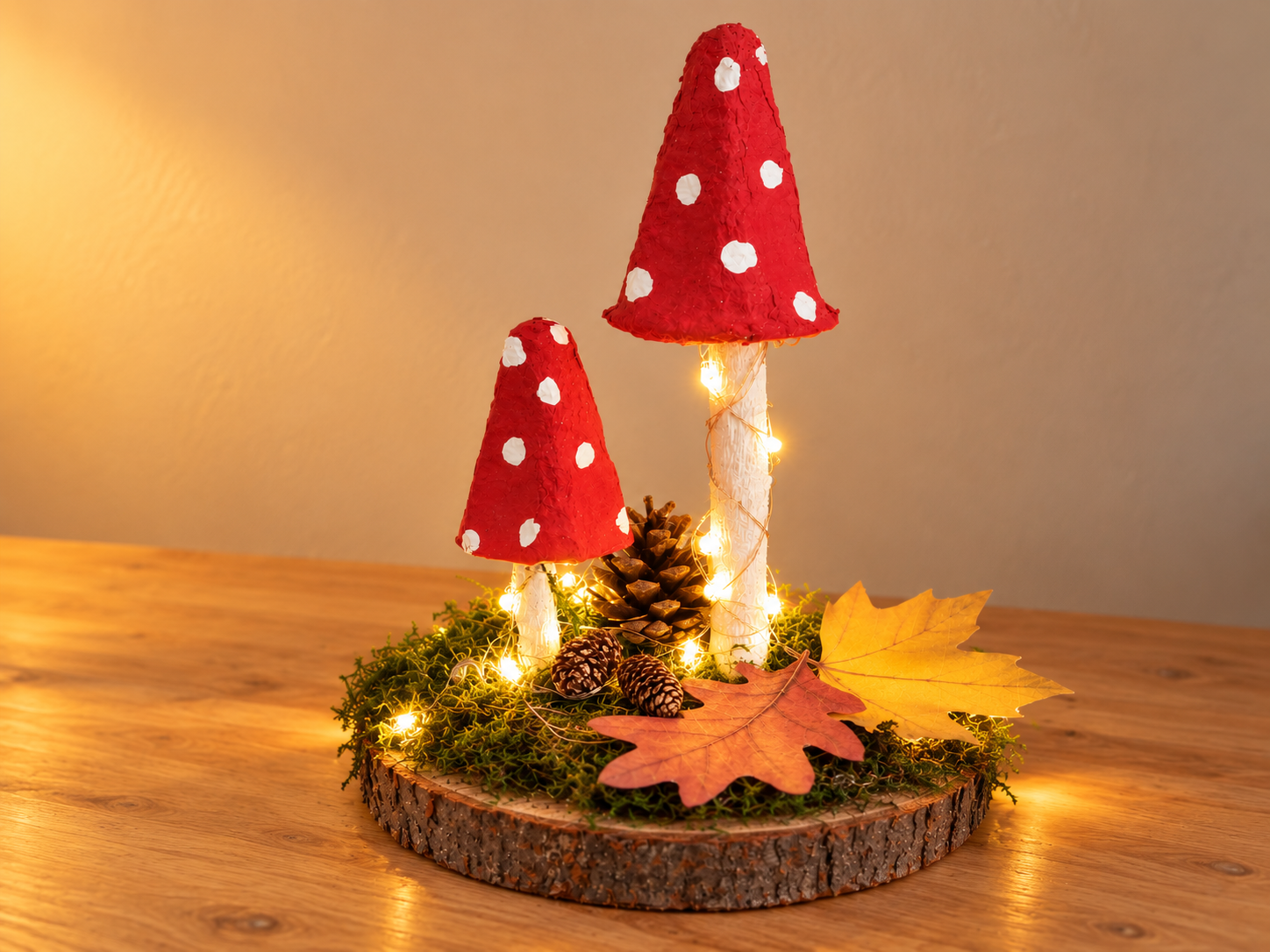 Beleuchtete selbst gebastelte Fliegenpilze auf einer Holzscheibe mit Moos, Zapfen und Herbstblättern.